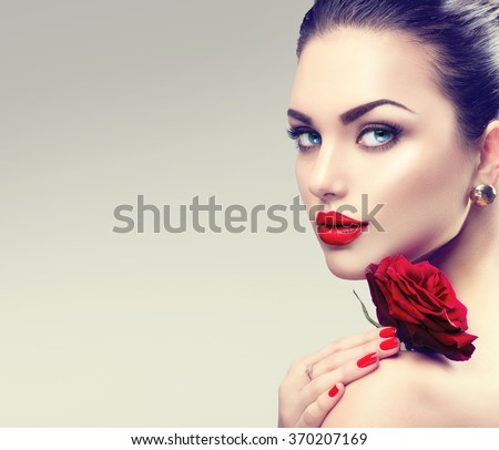 Beauty Fashion Model Woman face. Portrait with Red Rose flower. Red Lips and Nails. Beautiful Brunette Woman with Luxury Makeup and Manicure.