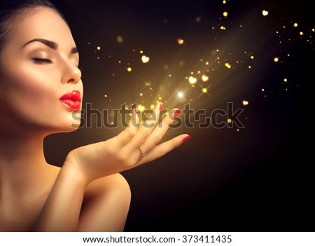 Beauty Young Woman Blowing Magic Dust with golden hearts and stars from her hands. Valentine's Day Holiday Concept. Isolated on black background Beautiful Romantic Girl. Miracle, magic of love