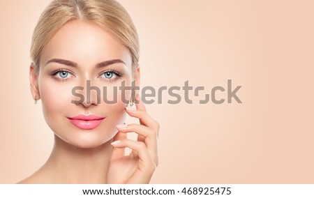 Beauty Woman face closeup Portrait. Beautiful Spa Girl Touching her Face and smiling. Perfect Fresh Skin. Pure Beauty Model Female looking at camera. Youth and Skin Care Concept. Beige background