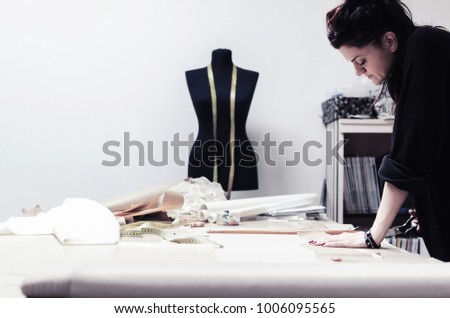 tailor cuts scissors, tailoring materials, professional female tailor using scissors and draft design cardboard on cloth material cut clothing design samples in production studio pattern table.