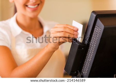 Cashier at work. Close-up of beautiful young female cashier swipes a plastic card through a machine