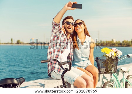 Collecting the bright moments. Smiling young couple making selfie while sitting on parapet near their bicycles
