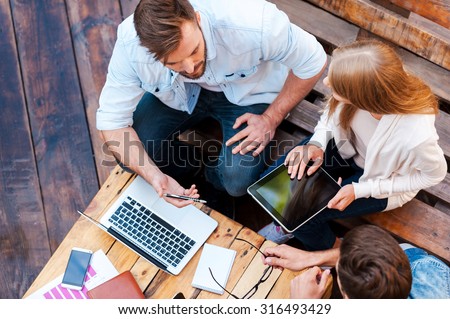 They can work anywhere! Top view of three young people working together while sitting outdoors