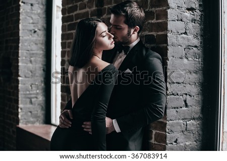 Beauty and passion. Beautiful young loving couple bonding to each other while both standing against brick wall indoors