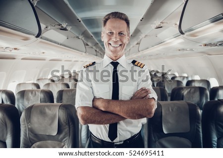 This is my plane. Confident male pilot in uniform keeping arms crossed and smiling while standing inside of the airplane