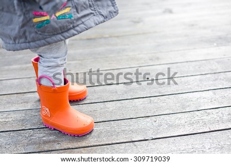 Baby in cute bright orange rubber boots on wood background