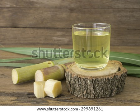 Freshly squeezed sugar cane juice in glass with cut pieces cane on a wooden table.