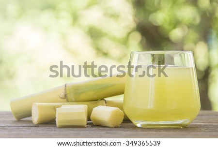 Fresh squeezed sugar cane juice in glass with cut pieces cane on nature background