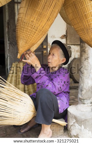 Hung Yen, Vietnam - July 26, 2015: Old woman weaves bamboo fish trap at Vietnamese traditional crafts village Thu Sy, Hung Yen province.