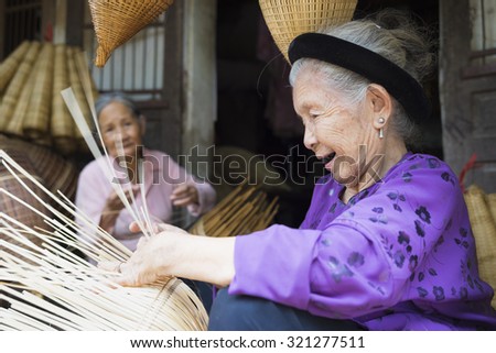 Hung Yen, Vietnam - July 26, 2015: Old woman weaves bamboo fish trap at Vietnamese traditional crafts village Thu Sy, Hung Yen province.