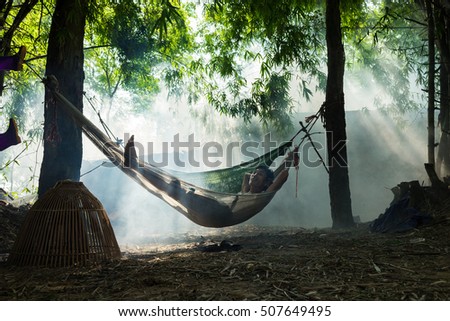 Bac Ninh, Vietnam - May 29, 2016: A man taking a break at noon on hammock in the shade of tree by Cau river