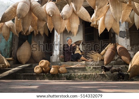 Hung Yen, Vietnam - July 9, 2016: Old house yard with many bamboo fish trap and female craftsman making traditional bamboo fish trap at her old house in Thu Sy trade village