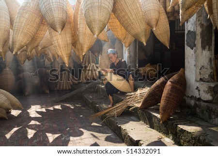 Hung Yen, Vietnam - July 9, 2016: Old house yard with many bamboo fish trap and female craftsman making traditional bamboo fish trap at her old house in Thu Sy trade village