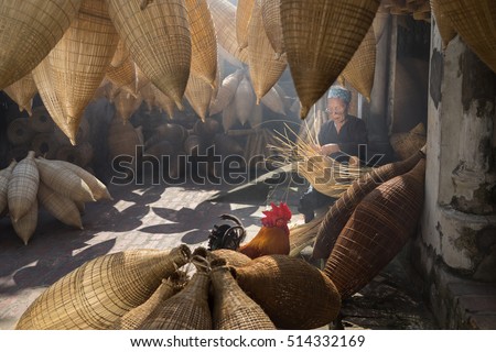 Hung Yen, Vietnam - July 9, 2016: Old house yard with many bamboo fish trap, cock, and female craftsman making traditional bamboo fish trap at her old house in Thu Sy trade village