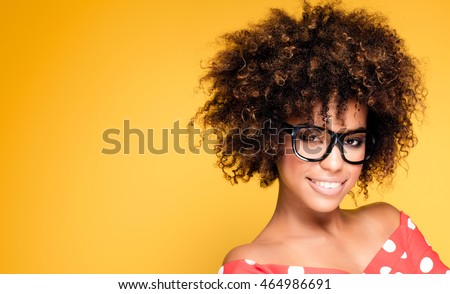 Portrait of smiling beautiful african american young woman. Girl with afro wearing eyeglasses. Yellow background. Studio shot.