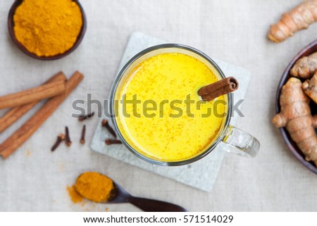 Turmeric drink, latte, tea, milk with cinnamon in a glass mug with fresh and dried turmeric on a textile grey background. Top view. Copy space.
