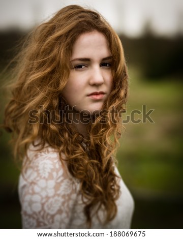 SAYKA stock photo portrait of a girl with long curly ginger hair outside in the wind against a green background 188069675