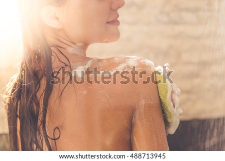 Cropped image of beautiful naked young woman smiling while taking shower in bathroom