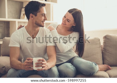 https://thumb7.shutterstock.com/display_pic_with_logo/2181548/598997255/stock-photo-beautiful-young-couple-is-talking-and-smiling-while-sitting-on-sofa-at-home-man-is-holding-a-cup-598997255.jpg