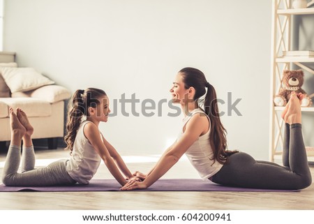 Beautiful young woman and her charming little daughter are smiling while doing yoga together at home