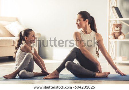 Beautiful young woman and her charming little daughter are smiling while doing yoga together at home