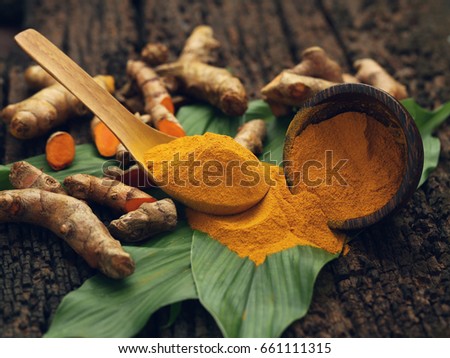 Turmeric powder and fresh turmeric on wooden background.
