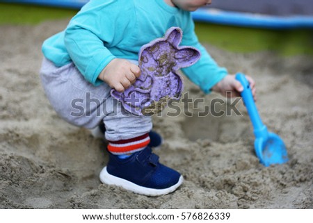 Children's outdoor play. A small child playing in a sandbox. In the hands of the baby scoop and mold for molding sand.
