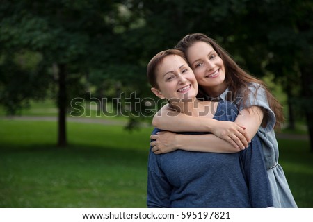 Mother and adult daughter hugging and having fun together in the park outdoor in summer. Portrait of happy women smiling and looking at the camera.