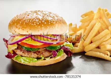 Unbearable desire. A closeup of a tempting tasty burger with red onion and vegs along with yummy french fries. - stock photo