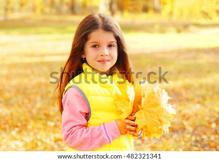 Portrait of beautiful little girl child with yellow maple leafs in autumn day