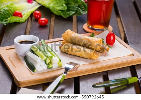 Spring rolls on wooden cutting board with glass of beer in soft focus on wooden table in restaurant. Close-up view.