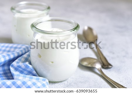 Two portions of fresh natural homemade organic yogurt in a glass jar on a light slate background.