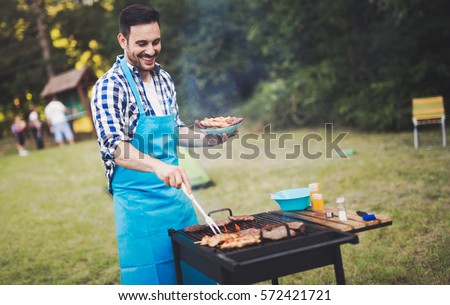 Handsome happy male preparing barbecue outdoors for friends