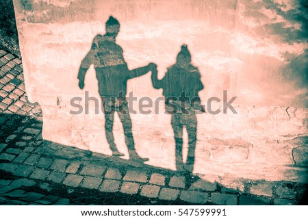 Happy couple shadow silhouettes in winter clothing holding their hands and walking against grunge old mauve pink wall and stone pavement background - Saint Valentine Day card backdrop