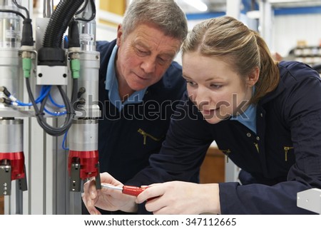 Engineer And Apprentice Working On Machine In Factory