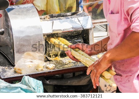 The man is squeezing juice from sugar cane.