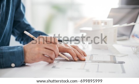 Professional architect working at office desk, he is drawing and making measurements on a project blueprint, engineering and architecture concept