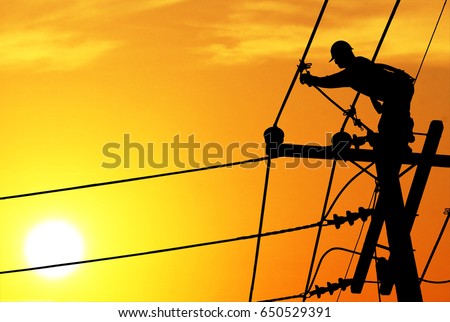 Shadow electricians repairing wire on electric power pole at the sunsetbackground blur.