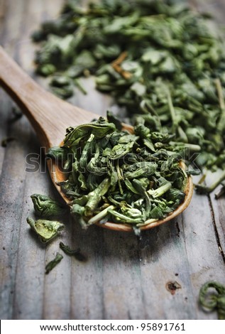 Spoon of dried green tea leaves on wooden background