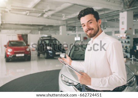 friendly vehicle salesman presenting new cars at showroom. Photo of young male consultant showing new car in auto show. Concept for car rental