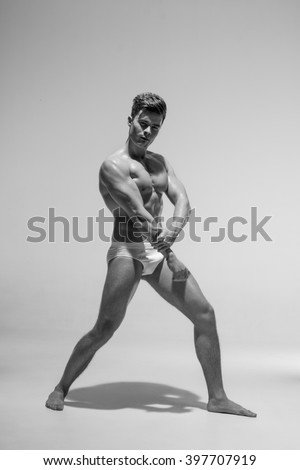 Beautiful athletic bodybuilder male model posing in studio. Muscular healthy sexy body. Expression on camera. Nude natural.