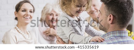 Little cute daughter standing n father's knees. Young mother and grandparents looking at her with smile and love