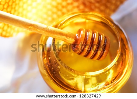 Honey dipper on the bee honeycomb background. Honey tidbit in glass jar and honeycombs wax.