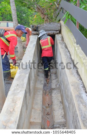 Muadzam Shah, Malaysia - March 22, 2018: Municipal workers "Alam Flora" uses sweepers and shovels to clean the garbage in the drain and put into the garbage bag.