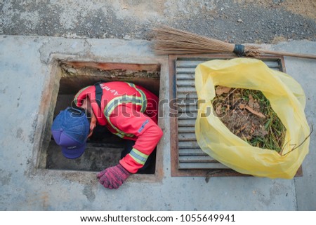Muadzam Shah, Malaysia - March 22nd, 2018: Municipal worker "Alam Flora" uses sweepers and shovels to clean the garbage in the drain and put into the garbage bag.