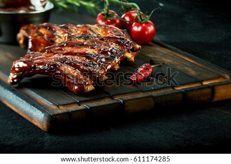 Rack of spicy barbecued chili spare ribs with a grilled cayenne pepper and tomatoes served on an old vintage wooden cutting board in a close up view