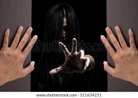 Halloween theme:Two woman hands opening a wooden door with ghost girl on black background.film filter effect. Halloween theme:Two woman hands opening a wooden door with ghost girl on black background.film filter effect.