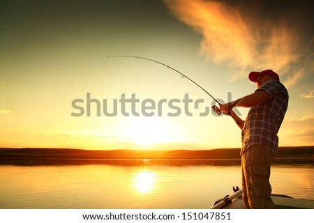 Young man fishing on a lake from the boat at sunset