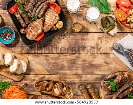 Outdoors Food Concept. Appetizing barbecued steak, sausages and grilled vegetables on a wooden picnic table with copy space, top view