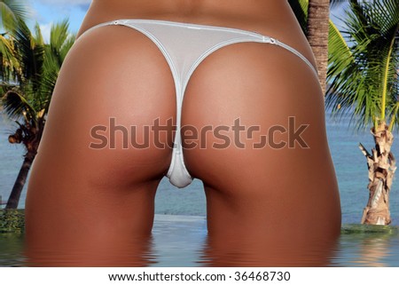 Beautiful skinny well tanned bottom with a white panty string in front of the ocean sea. Perfect female form and standing in the pool